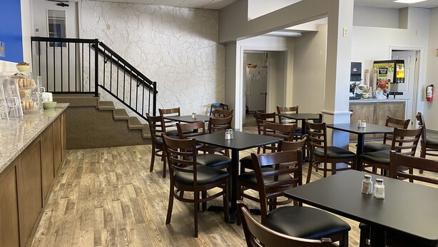 A dining area with wooden tables and chairs, a kitchen counter, and a staircase leading to another level. - SureStay by Best Western Brockville (Brockville)