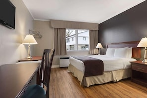 A hotel room with a bed, two bedside tables with lamps, a desk, a chair, a TV mounted on the wall, and a window with curtains.
