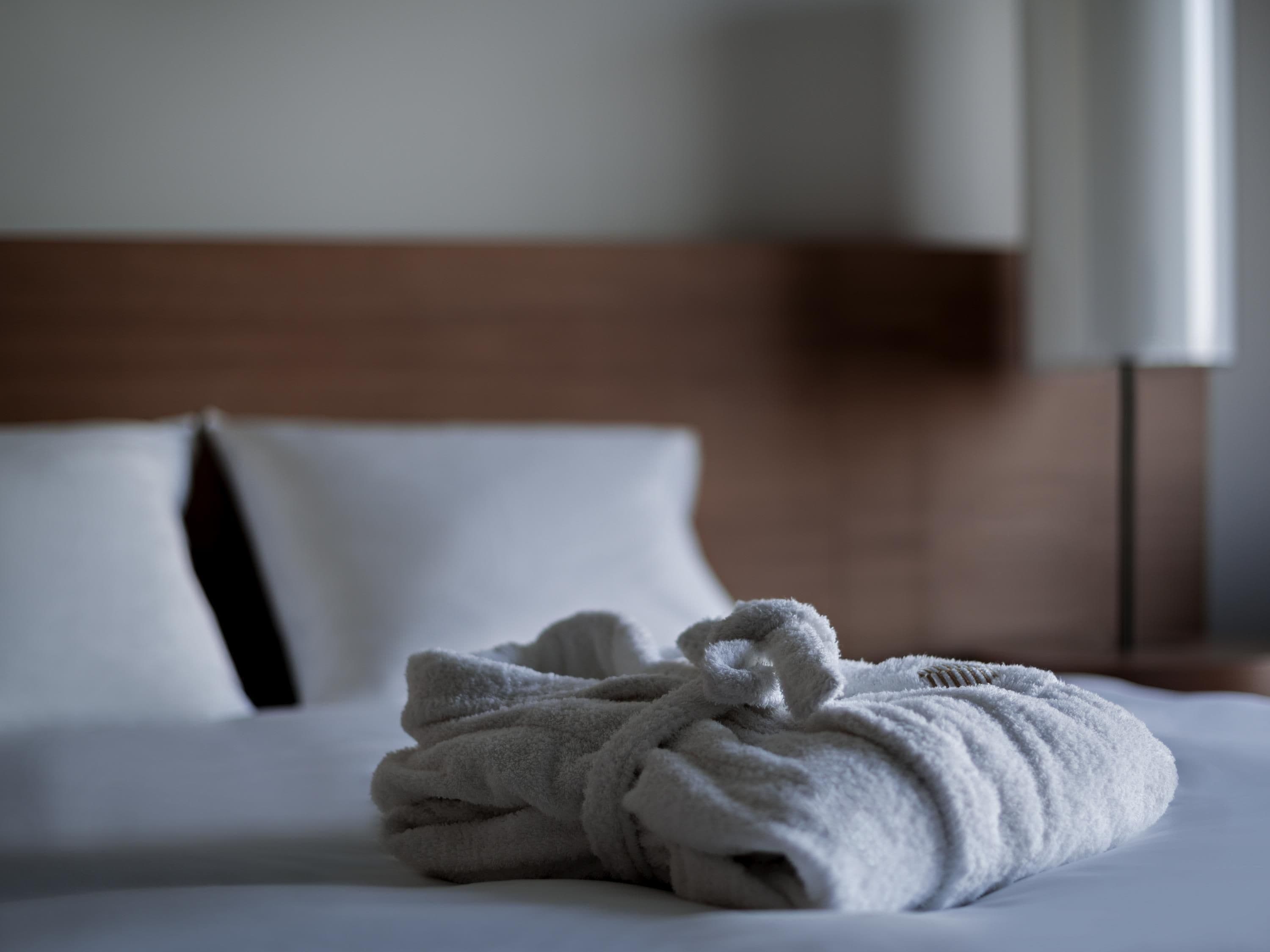A neatly made bed with a folded towel in the center.