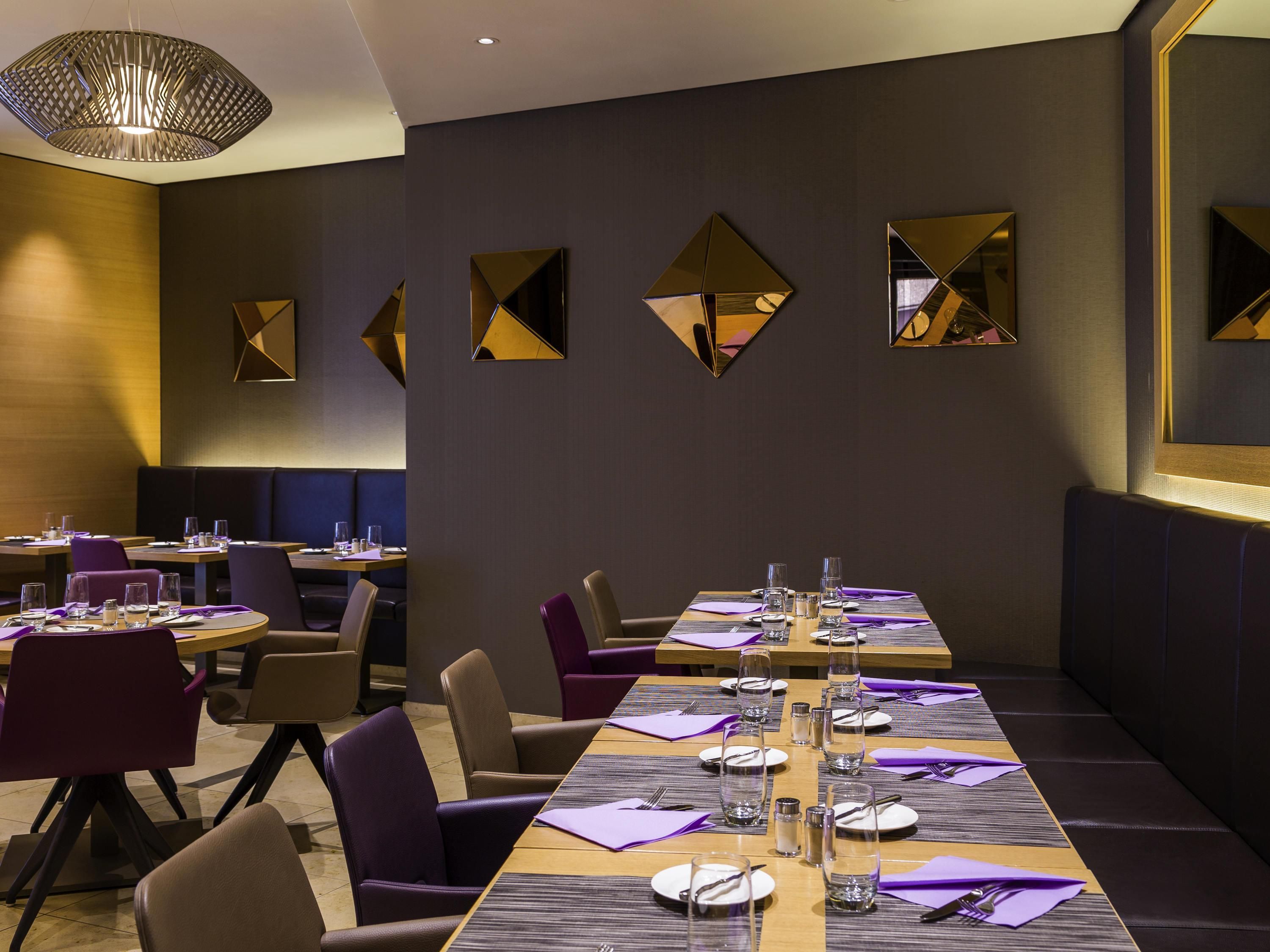 A modern dining area with a long table set for a meal, surrounded by chairs, and featuring geometric wall mirrors.