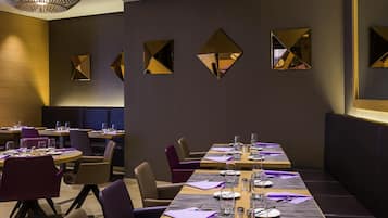 A modern dining area with a long table set for a meal, surrounded by chairs, and featuring geometric wall mirrors.