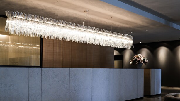 A modern reception area with a large, illuminated chandelier, a reception desk, and a seating area. - Pullman Basel Europe (Basel)