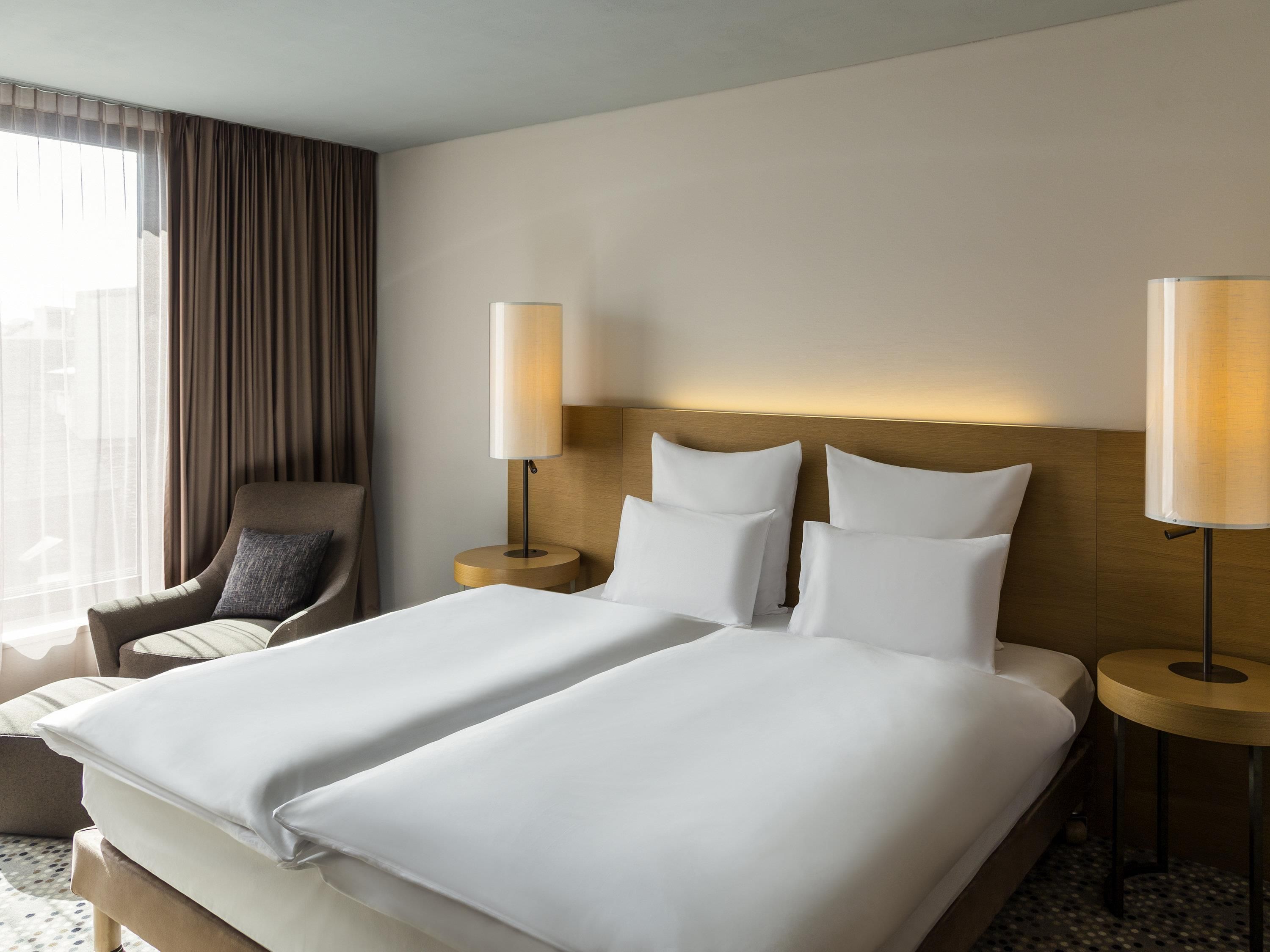 Une chambre d’hôtel avec un grand lit, deux tables de chevet, une chaise et une fenêtre avec des rideaux.