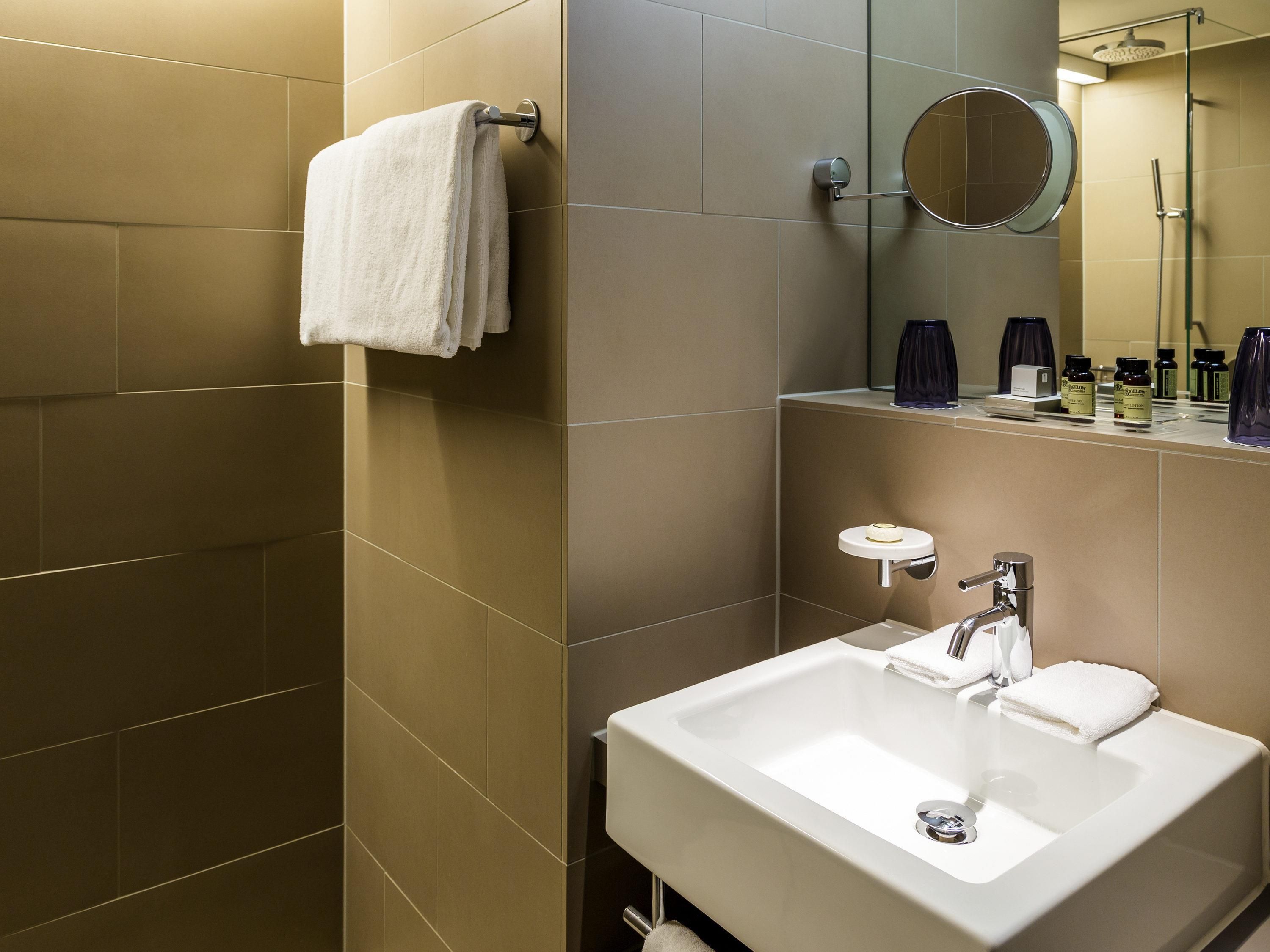 Un baño moderno con un lavamanos blanco, un perchero, un espejo y artículos de tocador sobre la encimera.