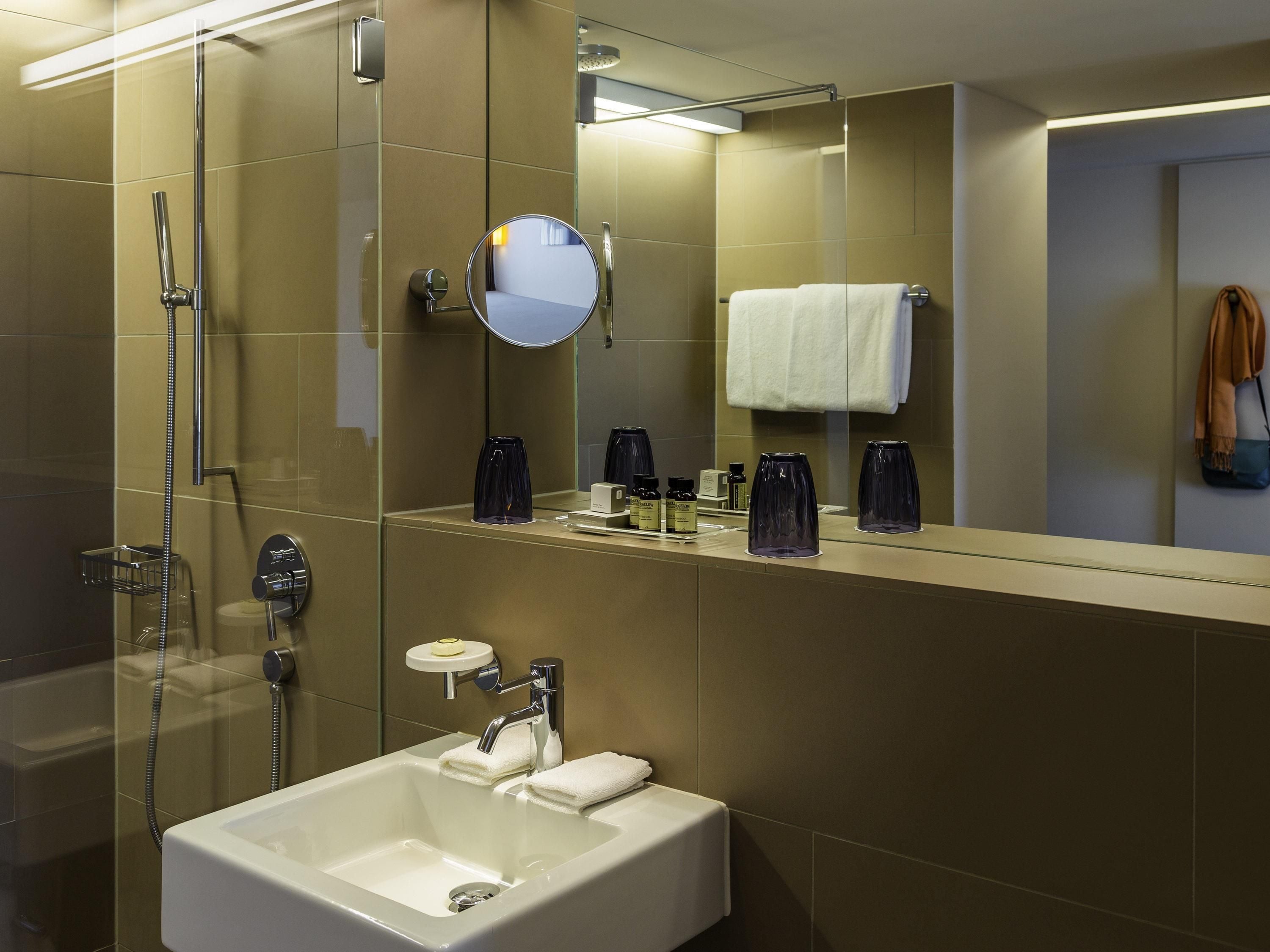 Une salle de bain moderne avec une douche à parois de verre, un lavabo avec un miroir et des articles de toilette posés sur le comptoir.