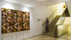 Un intérieur moderne agrémenté d’une installation artistique murale aux motifs géométriques, d’un escalier et d’un panneau indiquant les espaces réservés aux réunions et aux événements.
