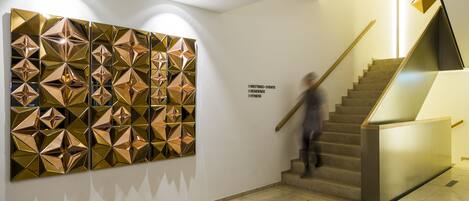 A modern interior with a geometric wall art installation, a staircase, and a sign indicating meeting and event spaces.