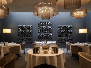 A dining area with round tables, gold serving dishes, and geometric wall art. - Pullman Basel Europe (Basel)