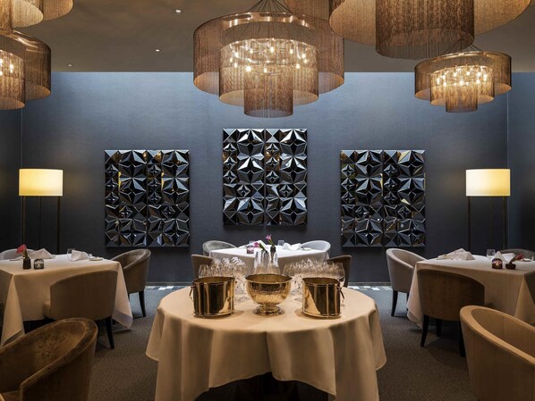 A dining area with round tables, gold serving dishes, and geometric wall art.