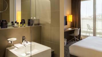 A hotel room with a large mirror, a white sink, a desk with a chair, a bed, and a balcony with a view.