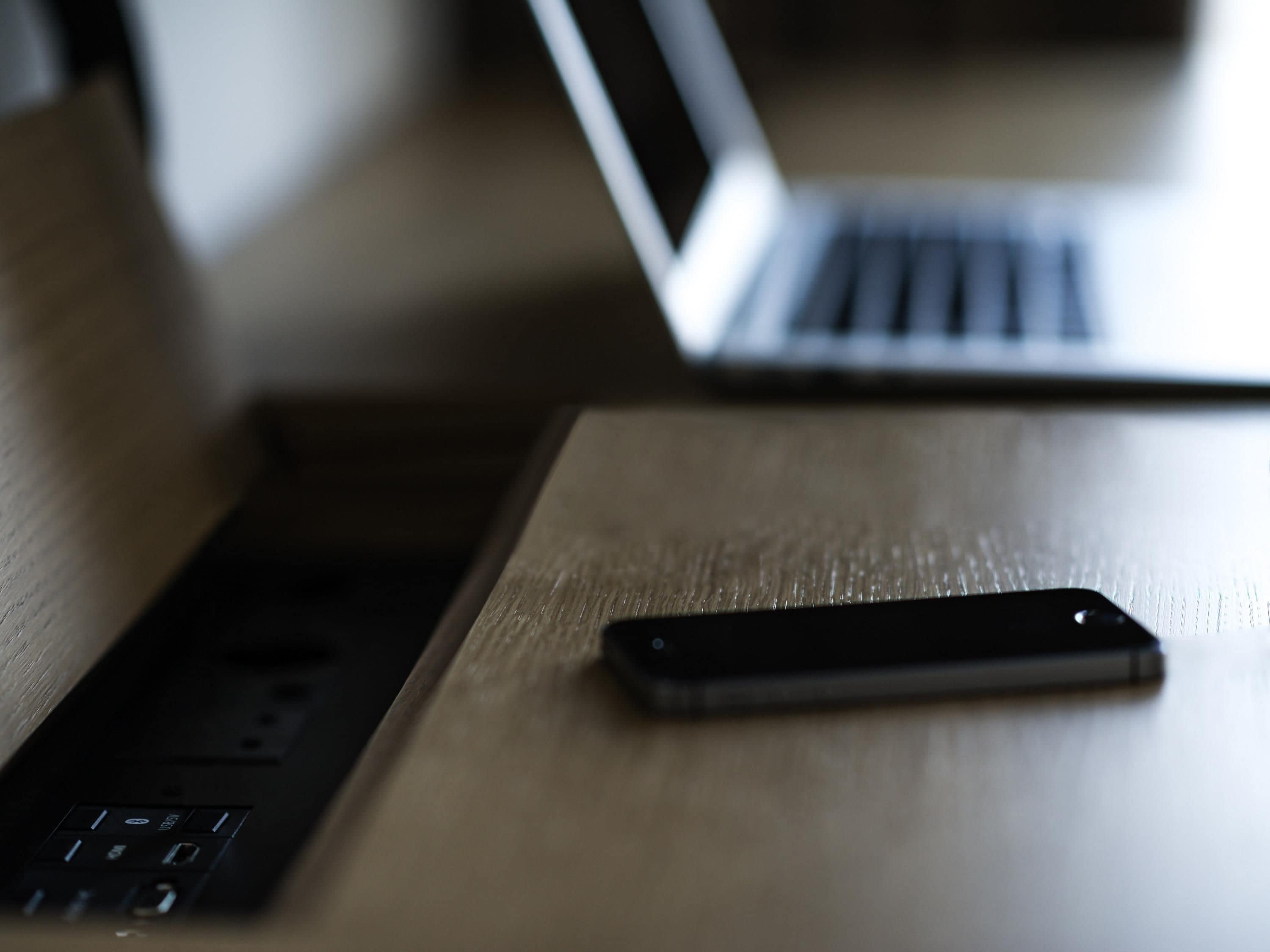 A wooden table with a smartphone and a laptop.