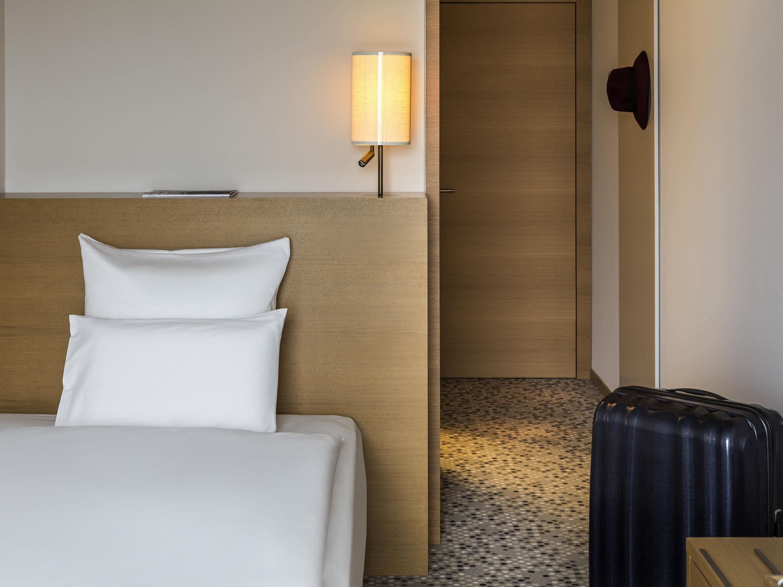 A hotel room with a bed, a lamp, a door, and a suitcase.