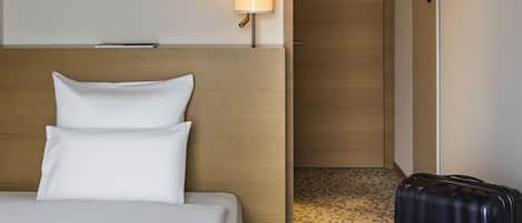 A hotel room with a bed, a lamp, a door, and a suitcase.