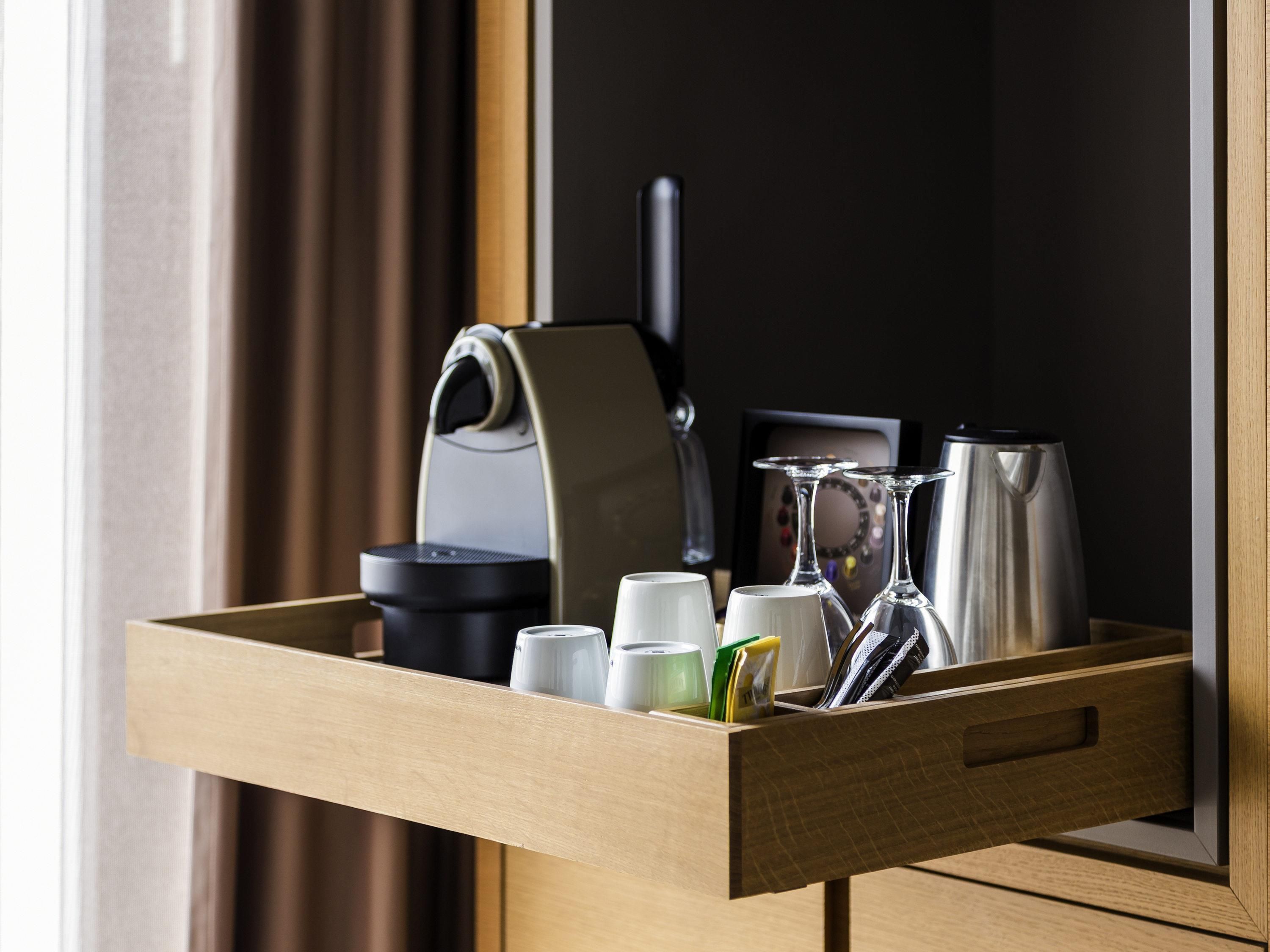 A wooden tray with a coffee maker, a kettle, and several cups and wine glasses.