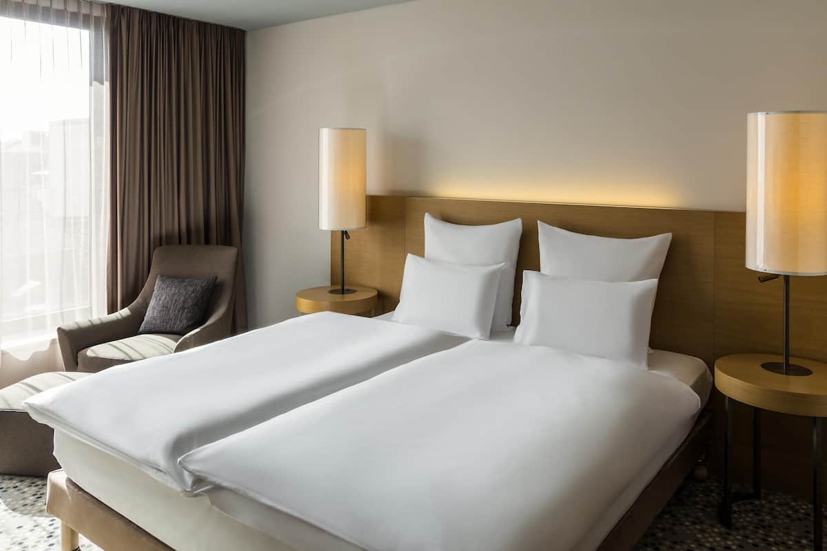 A hotel room with a large bed, two bedside tables, a chair, and a window with curtains.