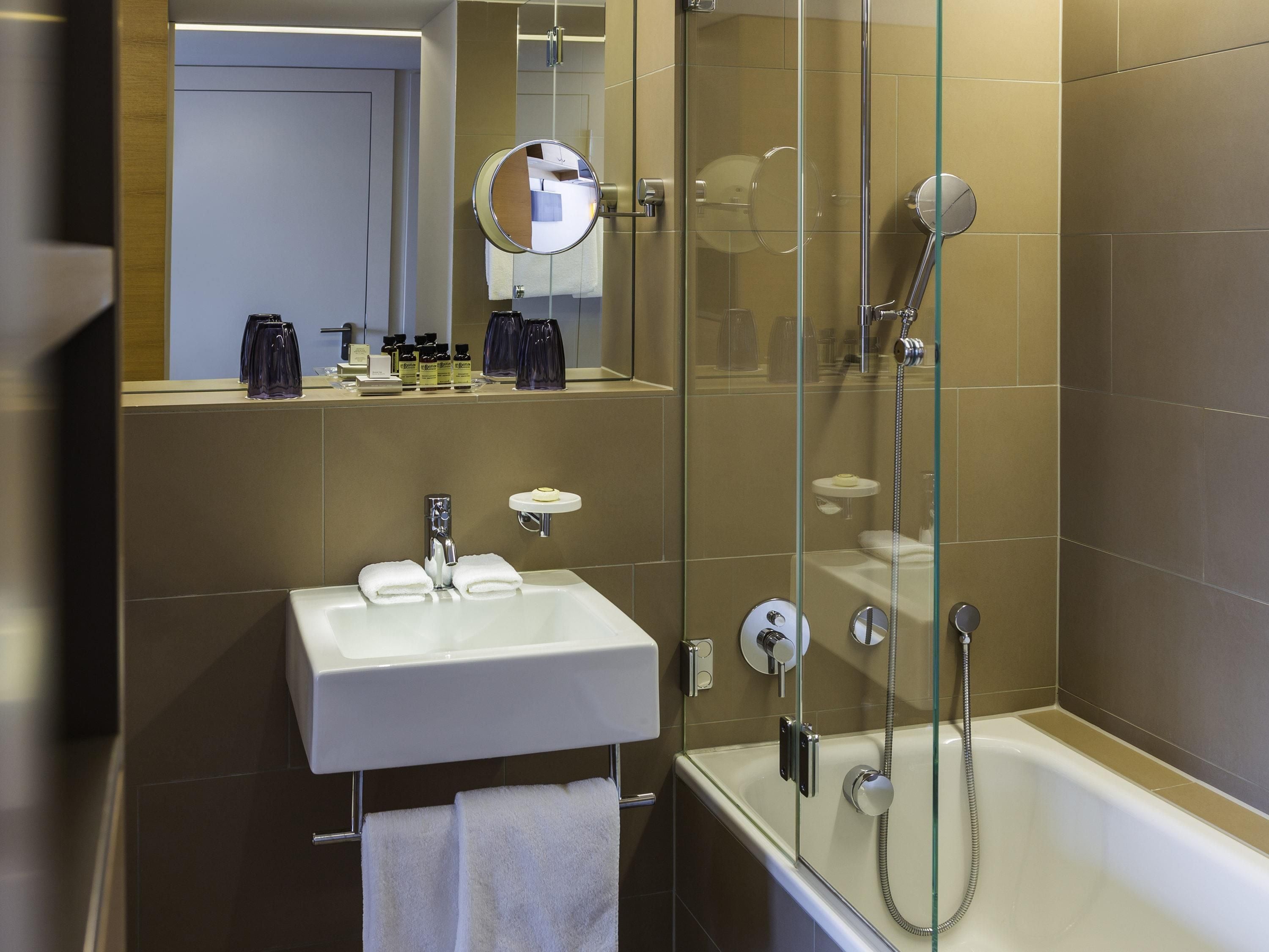 Un baño moderno con cabina de ducha de vidrio, un lavabo blanco con espejo y artículos de aseo en la encimera.