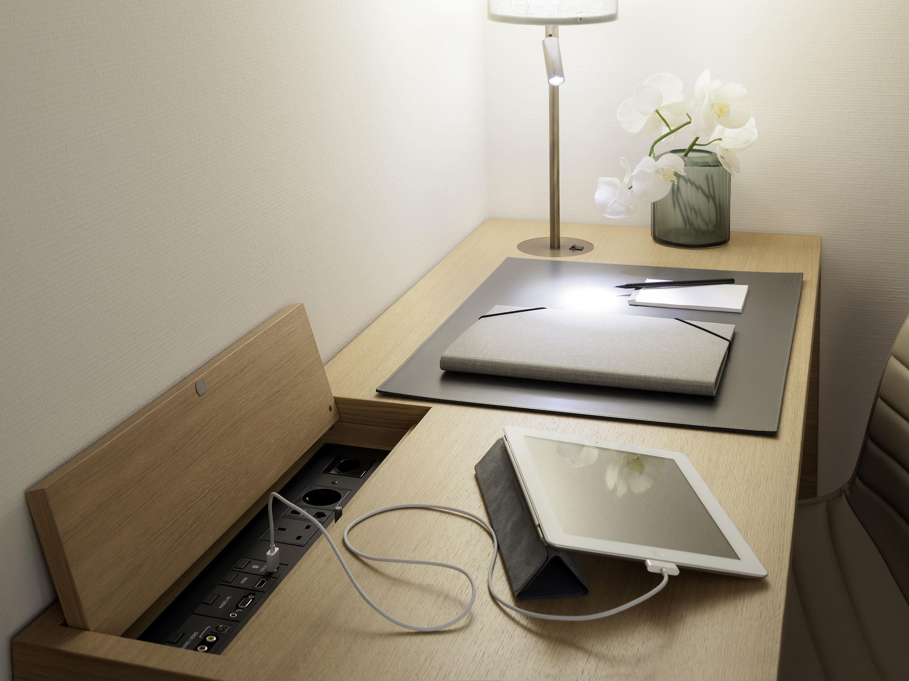 Ein ordentlicher Arbeitsplatz mit einem Laptop, einem Tablet, einer Lampe und einer Vase mit Blumen auf einem Nachttisch aus Holz.