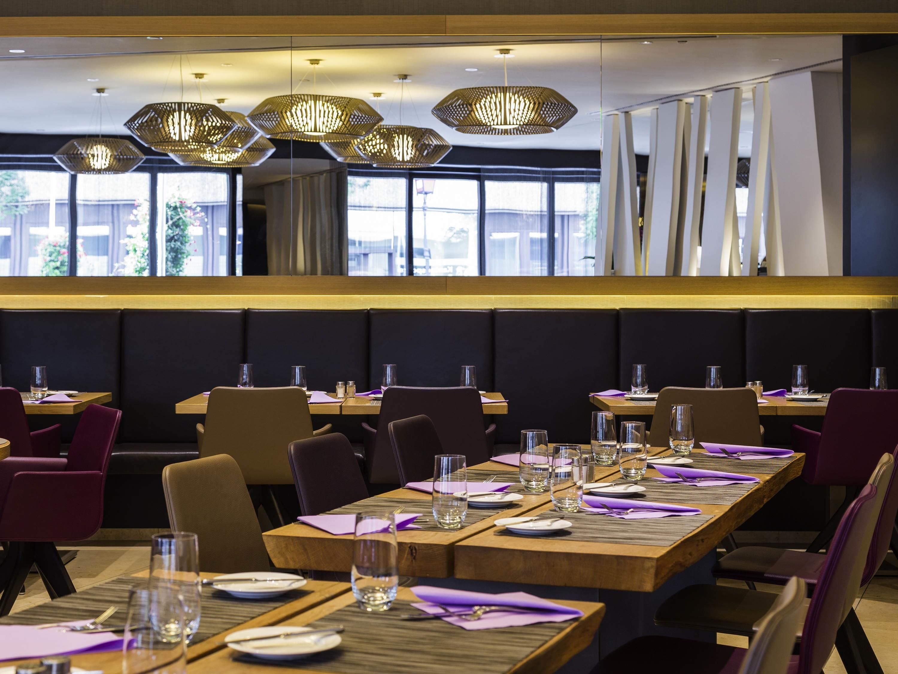 Een restaurant met houten tafels, paarse stoelen en hangende zeshoekige lampen.