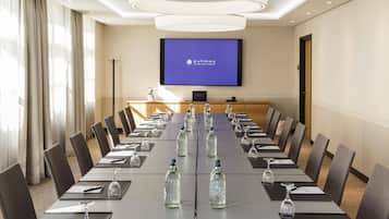 A conference room with a long table, chairs, water bottles, wine glasses, and a screen displaying 'Bonman'.