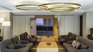 A modern lobby with a central coffee table, sofas, and a conference room with chairs. - Pullman Basel Europe (Basel)