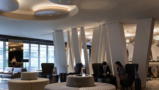 A modern lobby with a circular seating area, tall white columns, and a large window providing natural light. - Pullman Basel Europe (Basel)