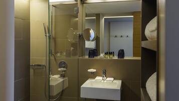 Un baño moderno con ducha acristalada, lavamanos con espejo y artículos de tocador sobre la encimera.
