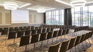 Une salle de conférence avec des rangées de chaises, un écran de projection et de grandes fenêtres.