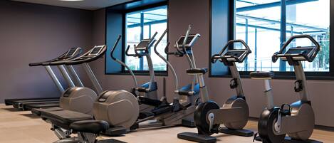 A gym with multiple cardio machines, large windows, and a modern design.