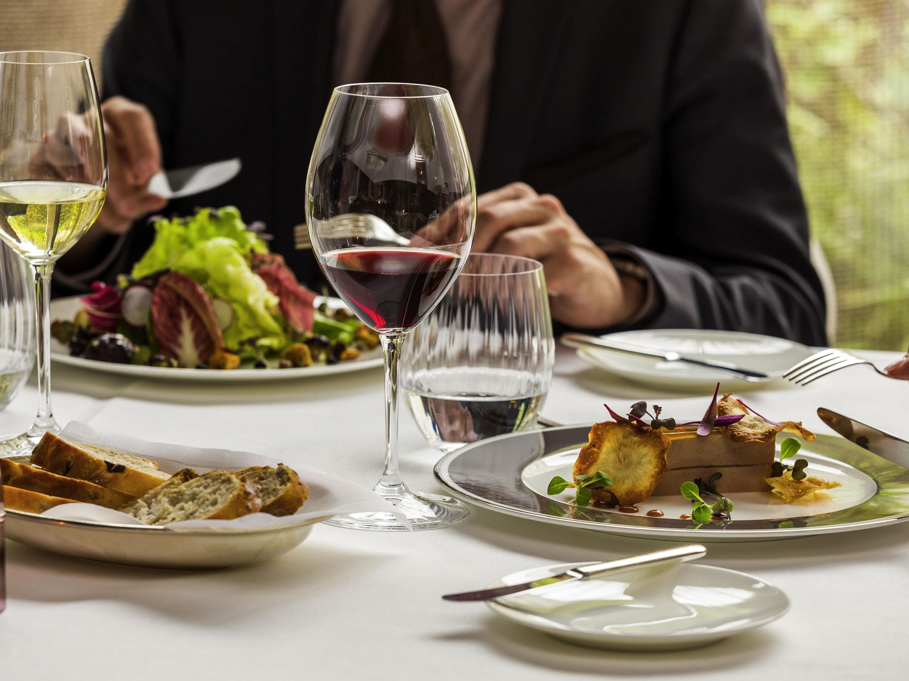 Una mesa de comedor con platos de comida, copas de vino y cubiertos.