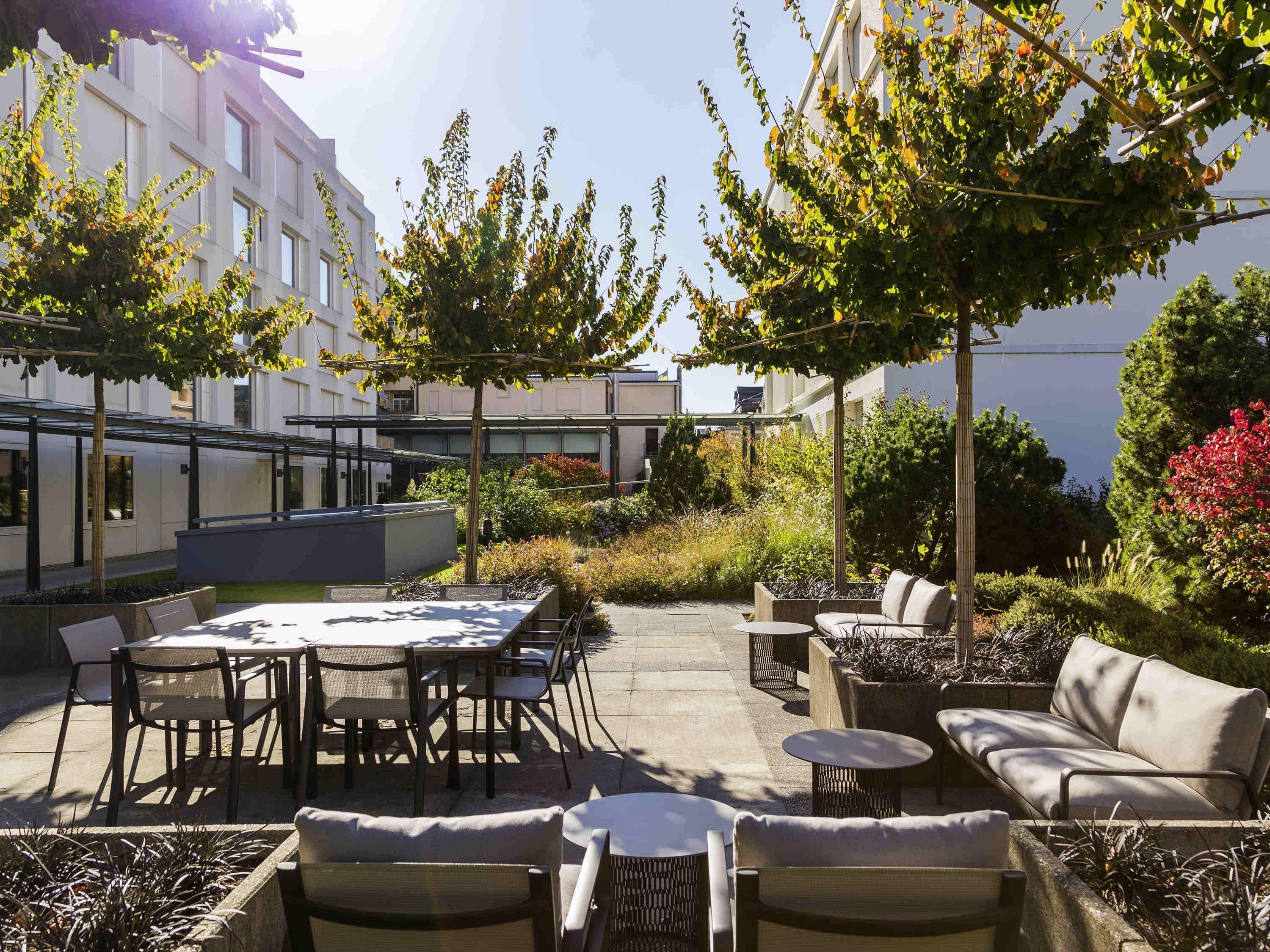 An outdoor patio with a dining table and chairs, surrounded by plants and a view of a building.