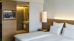 A hotel room with a bed, a bedside lamp, a mirror, and a small shelf with toiletries. - Pullman Basel Europe (Basel)