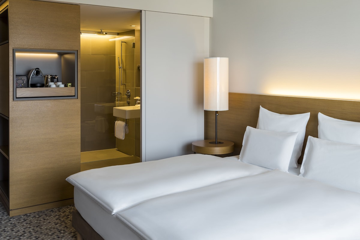 Une chambre d’hôtel avec un lit, une lampe de chevet, un miroir et une petite étagère contenant des articles de toilette.