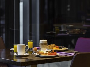 A breakfast table with plates of food, a glass of orange juice, a cup, and a glass of beer.