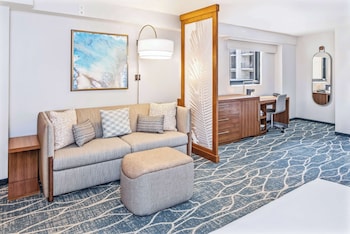 A hotel room with a large bed, a sofa, a small table, a chair, and a decorative wall panel. at Hyatt Place Waikiki Beach