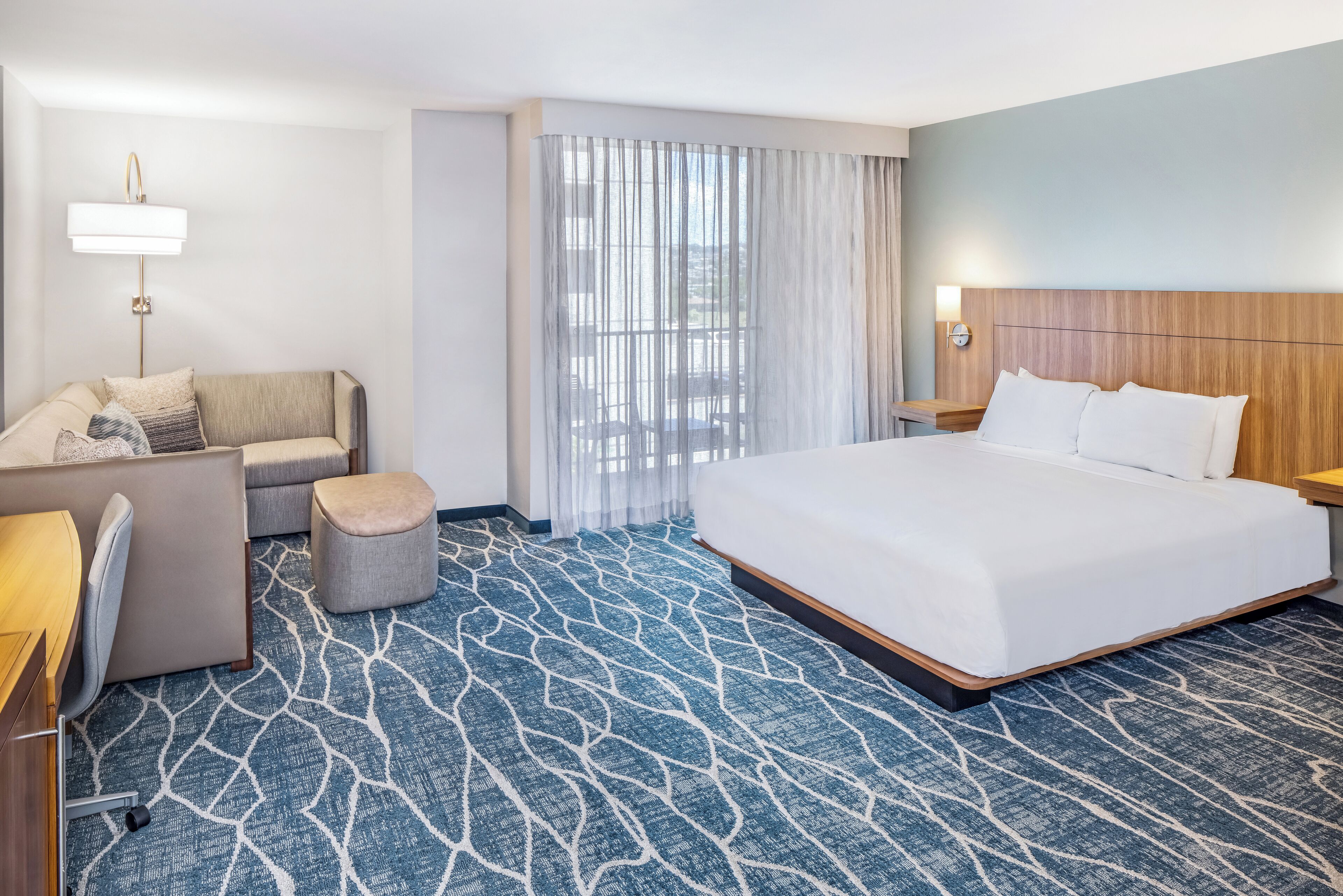 Habitación de hotel con una cama grande, un sofá, un escritorio y una ventana con cortinas.