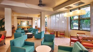 A spacious lobby with teal sofas, wooden tables, and a large window offering a view of greenery.