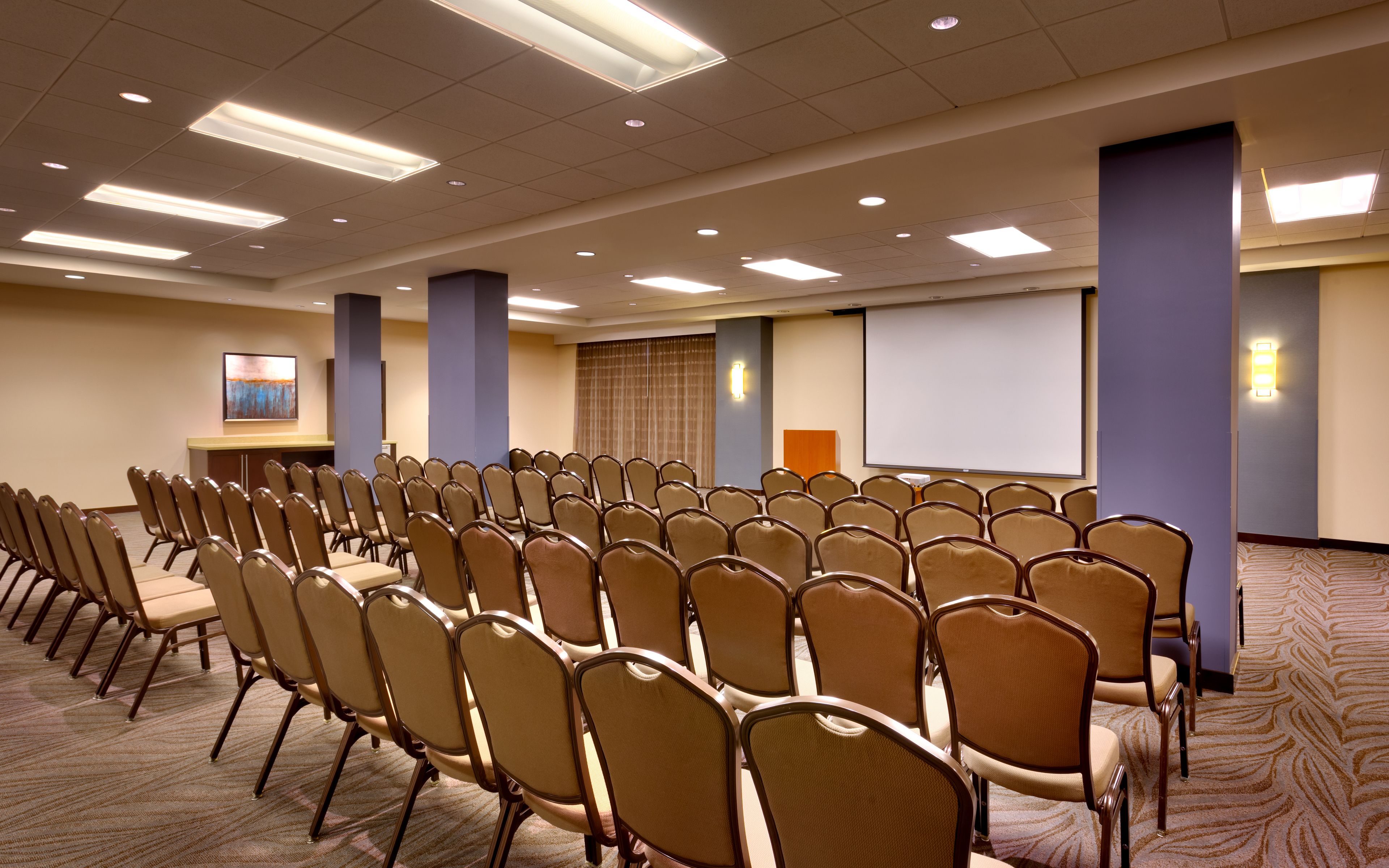 A conference room with rows of chairs, a projector screen, and a presentation podium.