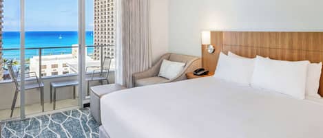 Habitación de hotel con una cama grande, una silla, un escritorio y vistas al océano.