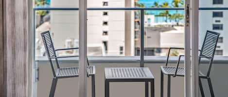 A balcony with two chairs and a small table, overlooking a cityscape and the ocean.