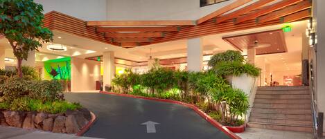 A modern indoor atrium with a central pathway, surrounded by greenery and wooden accents.