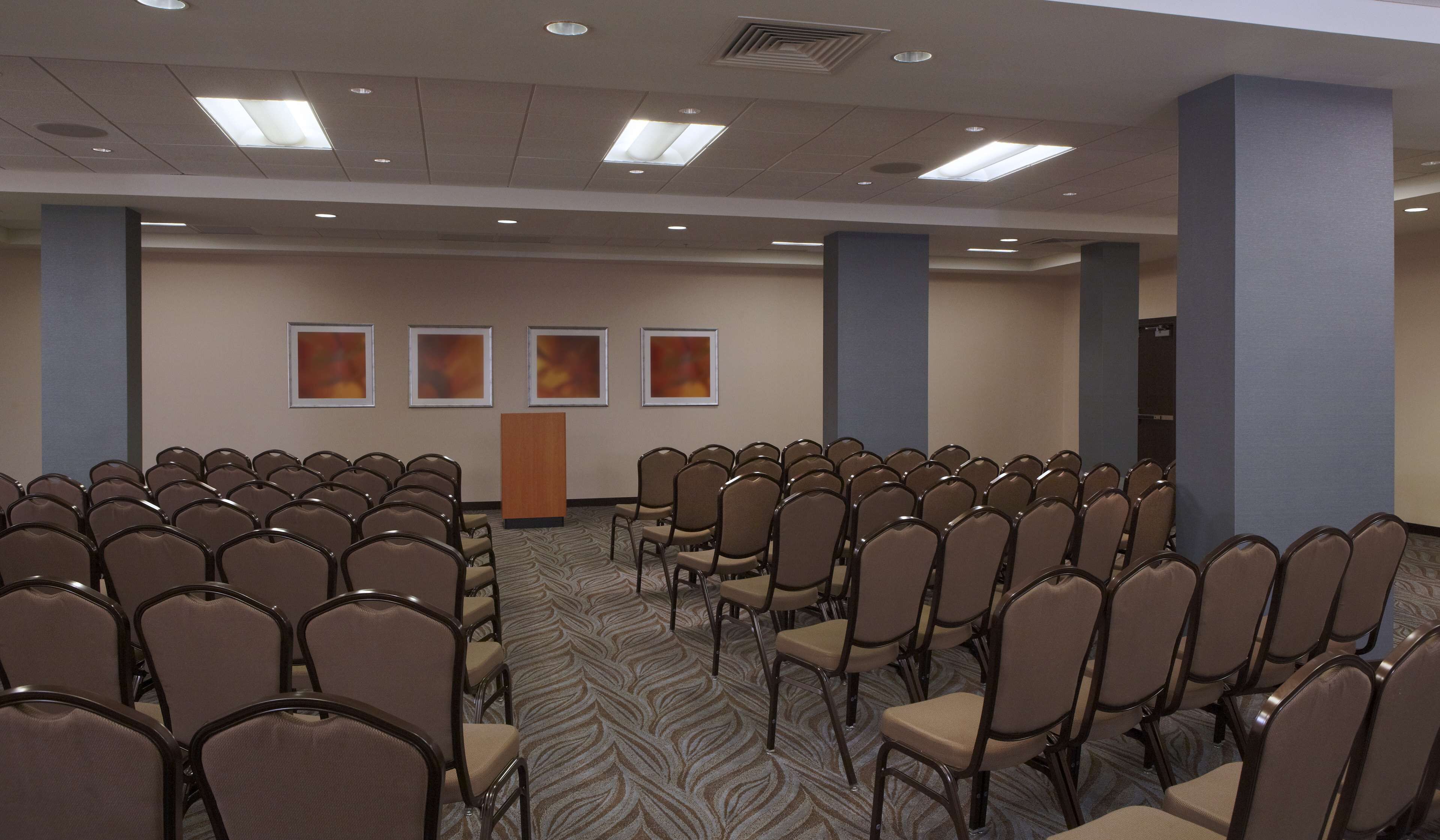 A conference room with rows of chairs, a podium, and framed pictures on the wall.