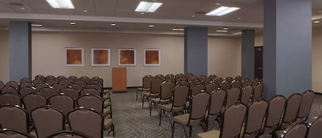 A conference room with rows of chairs, a podium, and framed pictures on the wall.