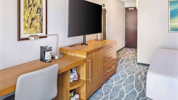 A hotel room with a wooden desk, a flat-screen TV, a coffee maker, and a minibar.