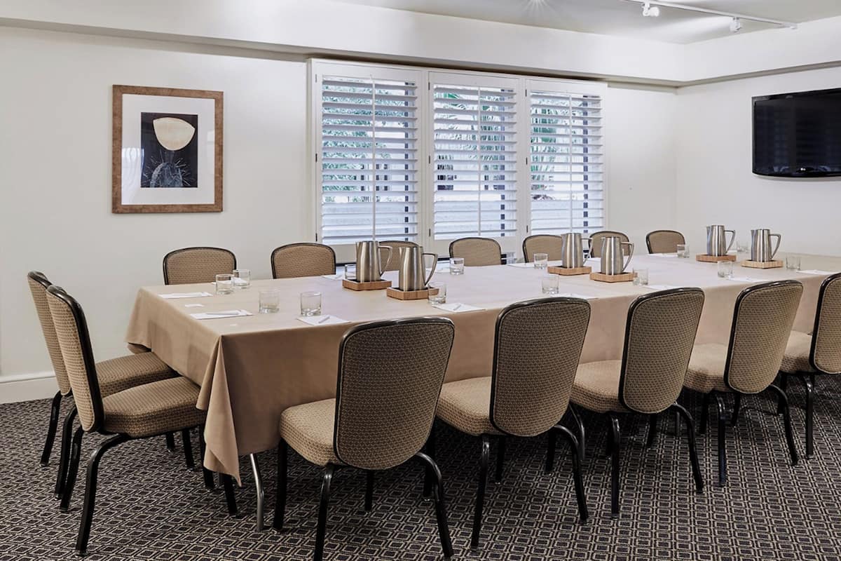 A conference room with a long table, chairs, a TV, and a window with blinds.