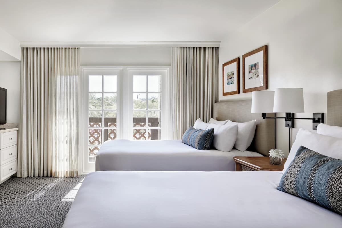 A hotel room with two beds, a TV, a nightstand, and a window with curtains.