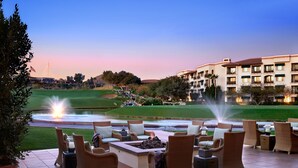 A patio with wicker furniture, a fire pit, and a view of a golf course and hotel buildings.