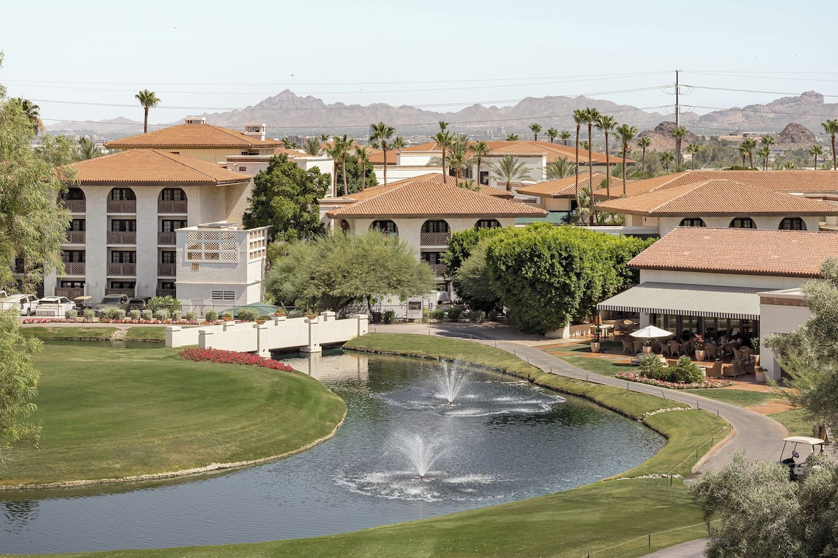 A golf course with a pond, palm trees, and buildings with red-tiled roofs.