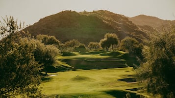 Un campo de golf con colinas ondulantes, árboles y una montaña al fondo.