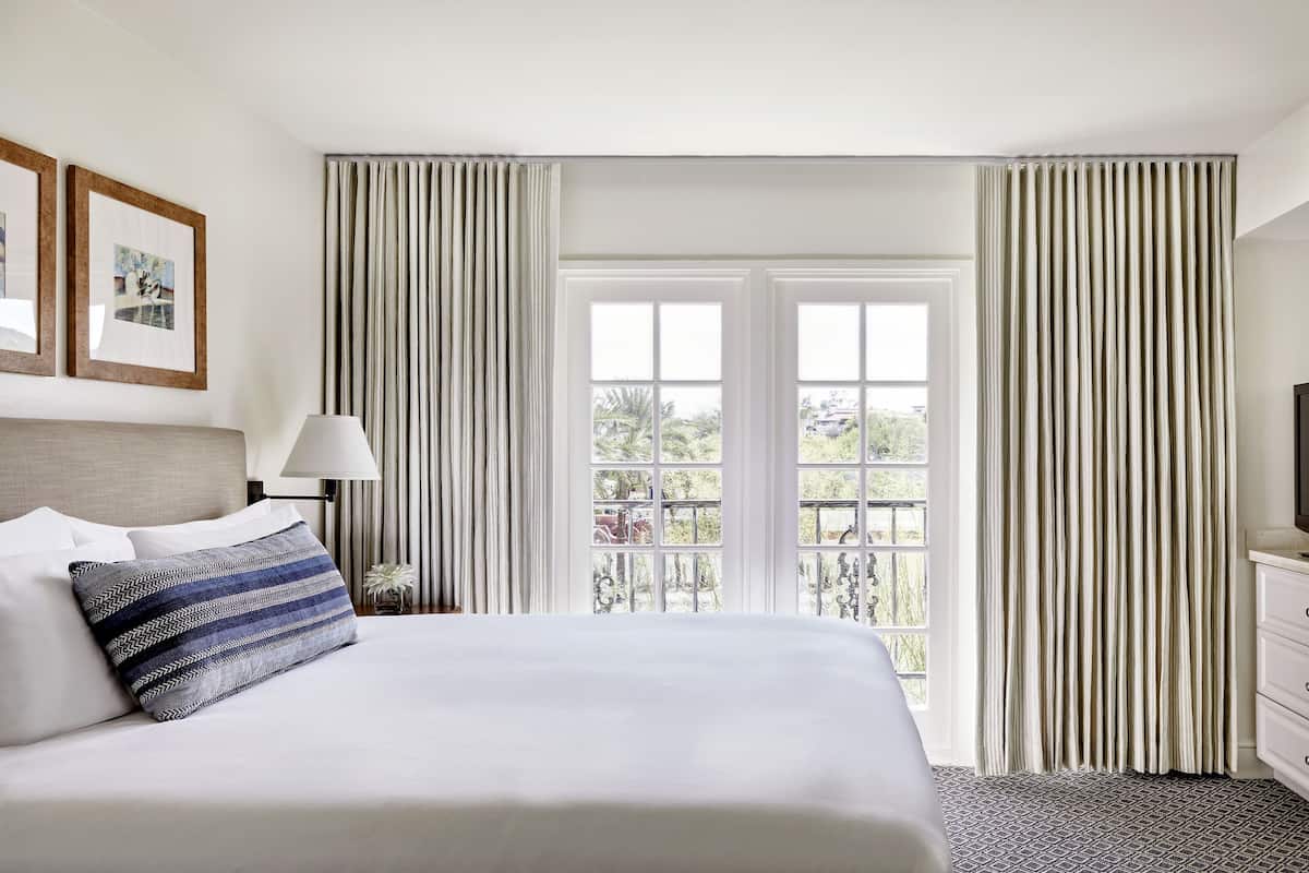 A hotel room with a large bed, a TV, and a balcony with curtains.