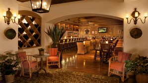 A bar area with wooden chairs and tables, a large potted plant, and a wine rack in the background.